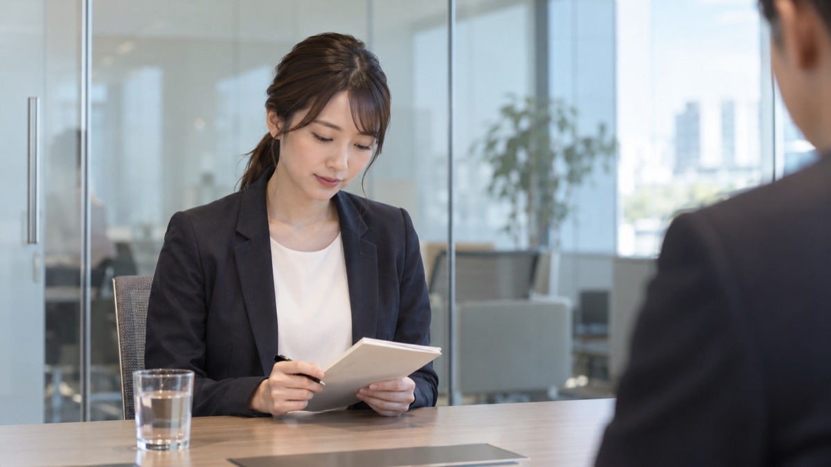 ガラス張りの面接室で、手元のメモに目を落としてひと呼吸おく30代の女性