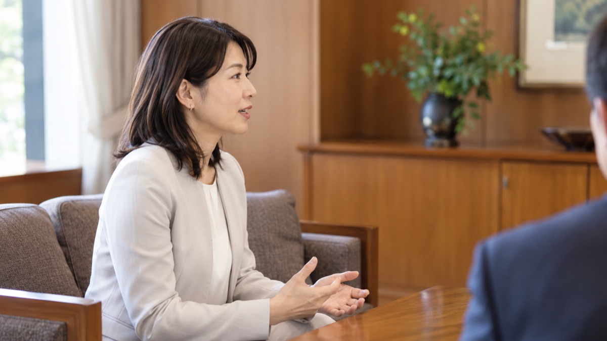 木目の家具の応接室で、ゆっくり区切りながら話す40代の女性の横顔