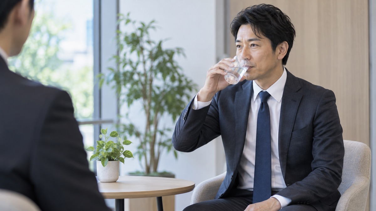 面接の途中、小さなテーブルで水を一口飲んで呼吸を整える40代の男性