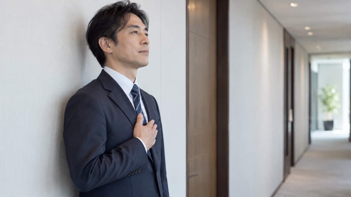 面接会場のビルの静かな廊下で、壁ぎわに立ち胸に手を当てて呼吸を整える40代の男性