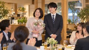 春の夕方、カフェレストランの歓送迎会で、花束を抱えた女性と新しく来た男性が並んで同僚の拍手を受けている