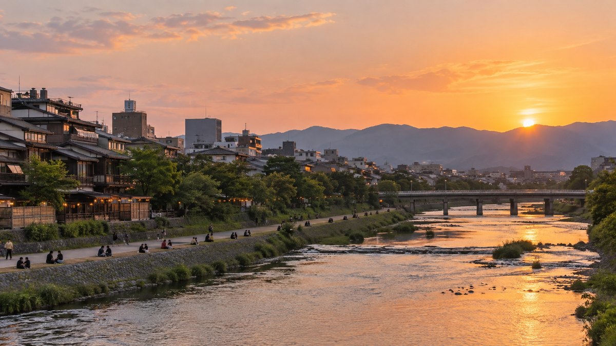 夕暮れの京都の鴨川の河原を、遠くから見た景色。川沿いに等間隔に座る人々は小さく写り、顔は分からない。看板の文字は写らない