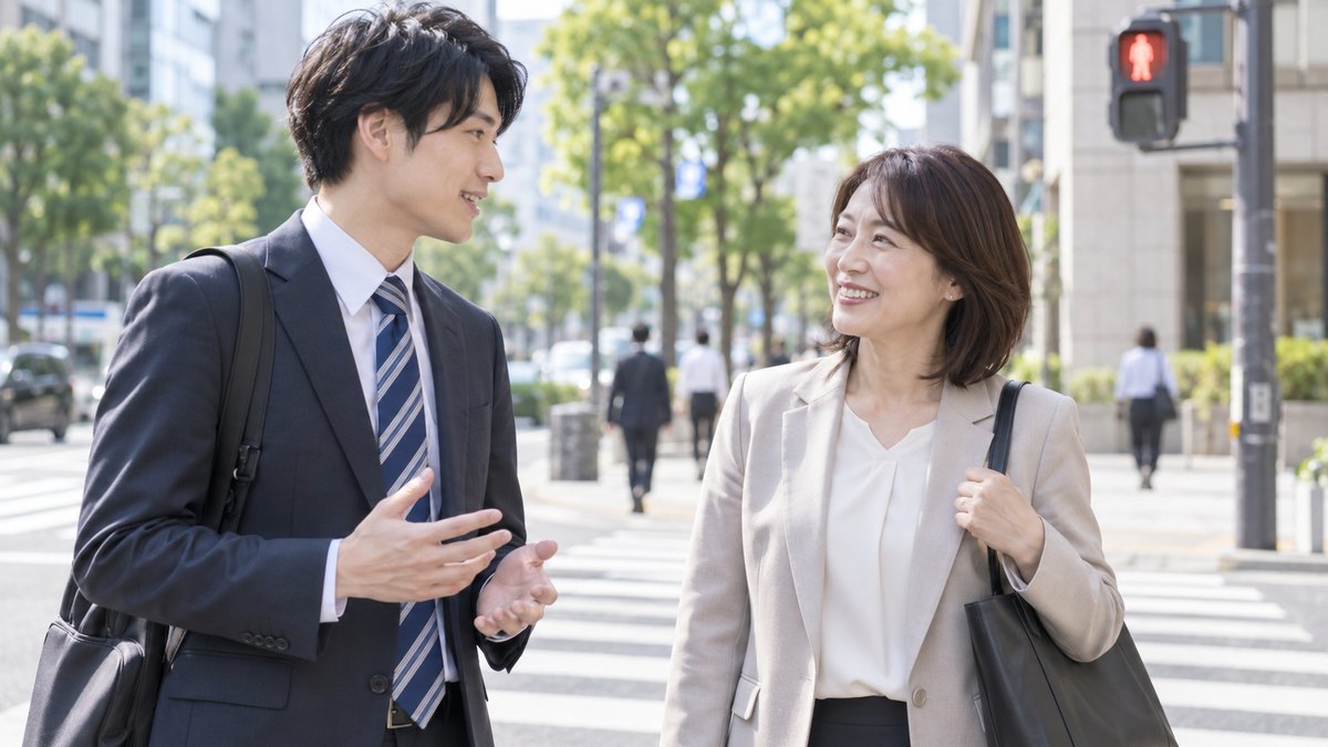 昼、会社の近くの横断歩道で信号を待ちながら、20代の男性社員が40代の女性の先輩に話しかけ、先輩が笑ってうなずいている