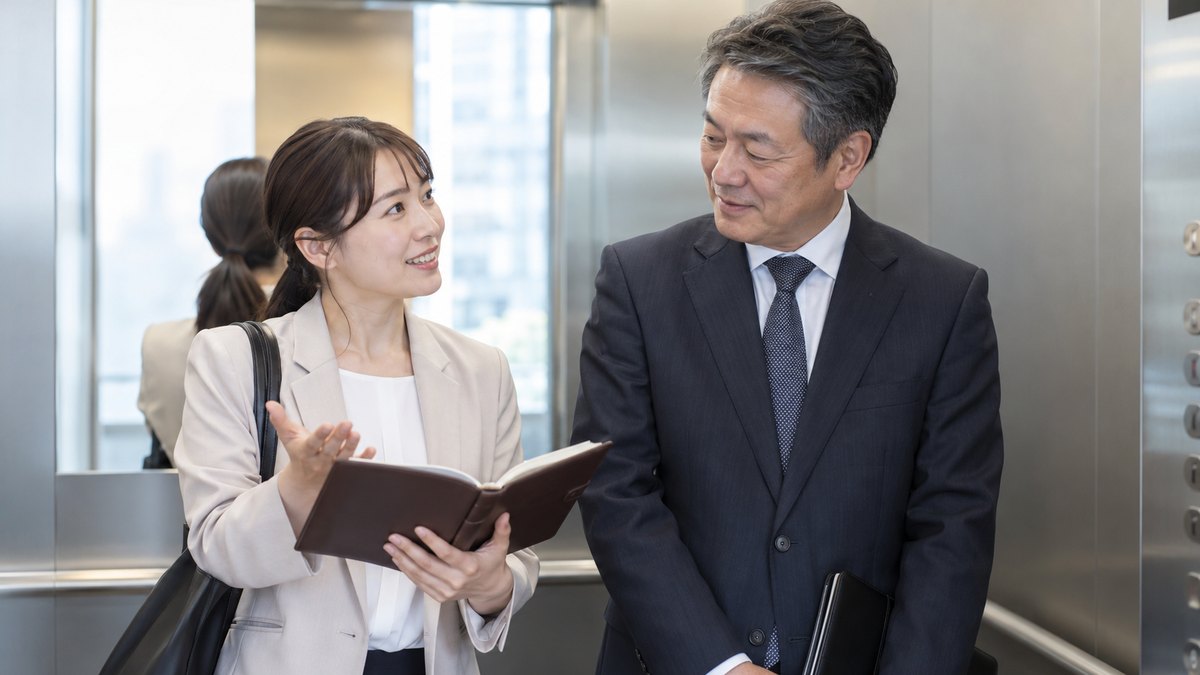 昼、会社のエレベーターの中で、幹事の30代の女性が手帳を開き、隣に立つ50代の男性部長に話しかけている。手帳や表示の文字は読めない